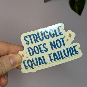 May include: A yellow sticker with a blue and white glittery design. The sticker says "Struggle does not equal failure".