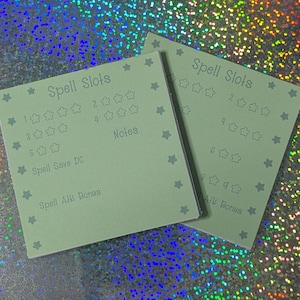 May include: Two light green cards with the text "Spell Slots" and star graphics. The cards have sections for tracking numbers and notes. The text "Spell Save DC" and "Spell Atk Bonus" are also visible.