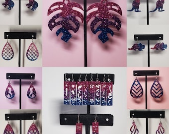 May include: Assortment of dangle earrings with various designs, including a monstera leaf, paw print, and a teardrop shape. The earrings are made of glitter and have a pink and blue ombre effect.