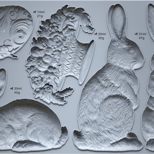 May include: A gray silicone mold featuring various rabbit designs and decorative floral elements. The mold includes rabbit profiles and a decorative basket. Measurements are indicated in milliliters and grams.