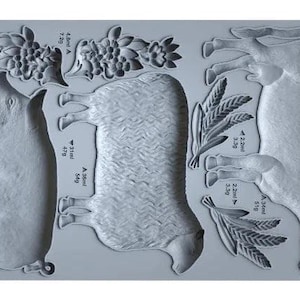 May include: A gray silicone mold featuring embossed farm animal designs, including a pig, sheep, and cow, along with floral and wheat elements. The mold is labeled "VILLAGE MARKET IOD" and includes volume and weight measurements.