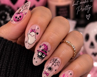 May include: Almond-shaped nails featuring light pink polish and Halloween-themed nail stickers. Designs include a pink pumpkin, a white ghost with a pink bow, a black soot sprite in a purple witch hat, a spider with a web, and pink drips.