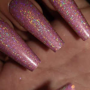 May include: Close-up of three long, pink, iridescent nails with a glittery finish.