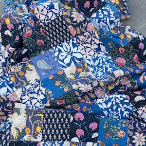 Peut inclure: Une courtepointe patchwork avec divers motifs floraux et cachemire dans des tons de bleu, blanc, rose et jaune. La courtepointe est composée de plusieurs carrés de tissu cousus ensemble, créant un design visuellement intéressant.