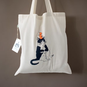 Sac fourre-tout chat orange | Illustration sérigraphiée à la main d'un chat équilibrant des oranges sur un sac en coton biologique naturel avec du bleu marine et de l'orange fluo