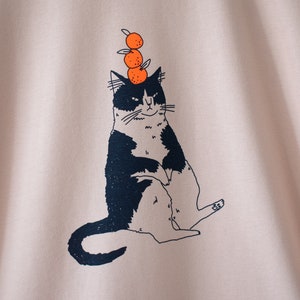 Oranje Kat t-shirt Met de hand gezeefdrukte illustratie van een kat die sinaasappels balanceert op een mistig roze T-shirt van biologisch katoen met marineblauw en oranje afbeelding 2