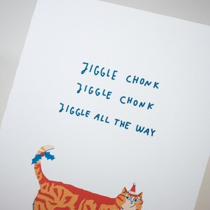 May include: A white card with the text "Jiggle Chonk Jiggle Chonk Jiggle All The Way" in blue handwriting. A cartoon orange and white cat with a red Santa hat and holly on its tail is at the bottom of the card.