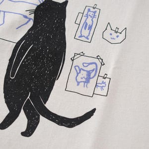 Cat gallery t-shirt | Hand screen printed on beige organic cotton tee with black and blue illustration of a cat judging his own art image 8