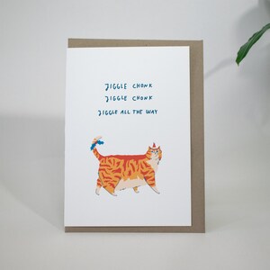 May include: A greeting card with a cartoon orange and red tabby cat wearing a blue and white party hat. The text on the card reads "Jiggle Chonk Jiggle Chonk Jiggle All The Way."