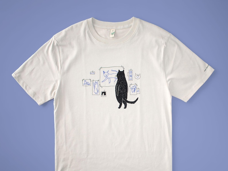 Cat gallery t-shirt | Hand screen printed on beige organic cotton tee with black and blue illustration of a cat judging his own art image 1