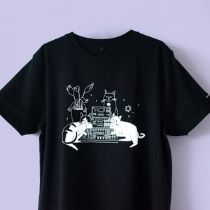 シンセサイザーに座る猫のTシャツ | 黒のオーガニックコットンTシャツに水性ホワイトインクでスクリーンプリントされたDJ猫のイラスト