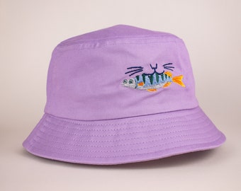 Eaty the fishy cat bucket hat | Lavender cotton hat with blue, green and orange embroidered illustration of a cat eating a bass