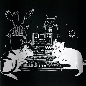 T-shirt de chats assis sur un synthétiseur Chats dj cats illustrés sérigraphiés sur un t-shirt en coton biologique noir avec de l'encre blanche à base d'eau image 2