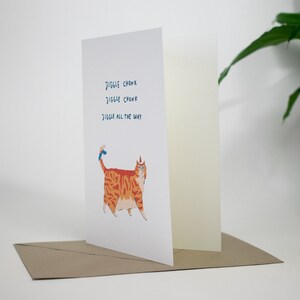 May include: A greeting card with a cartoon orange cat wearing a blue party hat. The text on the card reads "Jiggle Chonk Jiggle Chonk Jiggle All The Way".