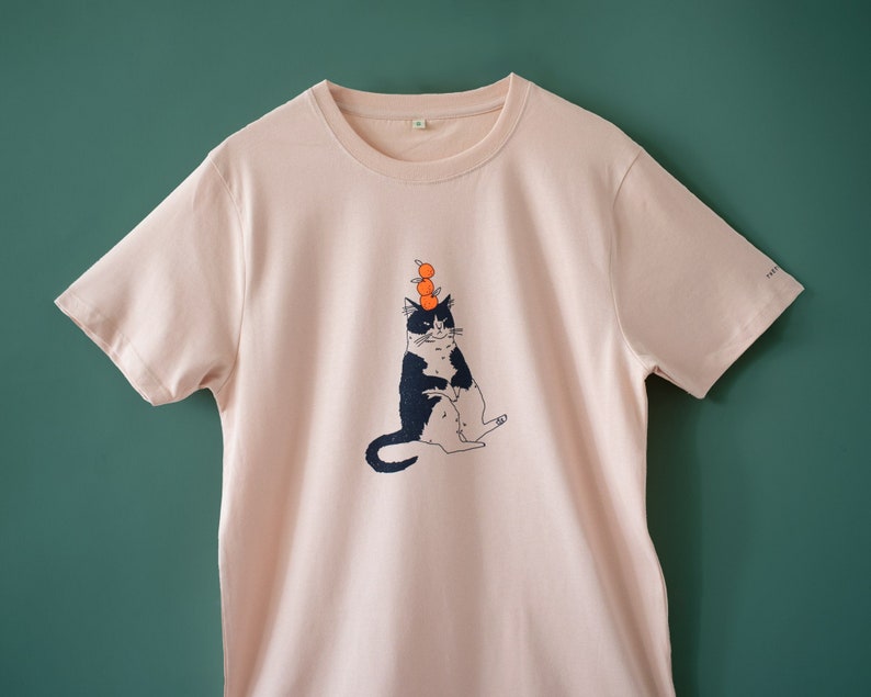 Oranje Kat t-shirt Met de hand gezeefdrukte illustratie van een kat die sinaasappels balanceert op een mistig roze T-shirt van biologisch katoen met marineblauw en oranje afbeelding 1