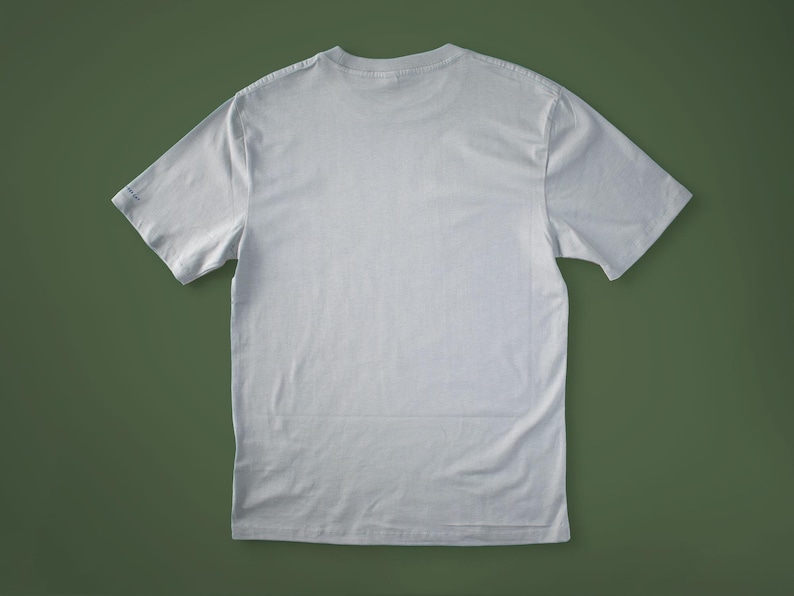 May include: A light gray, short-sleeved t-shirt, viewed from the back, lies on a green surface. The shirt has a crew neck and a simple, classic design, suitable for casual wear.