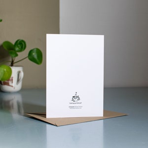 May include: A white card with a black and white illustration of a cat wearing a party hat. The text "theprintcat" is printed below the illustration, along with the text "instagram: @theprintcat" and "www.theprintcat.com".