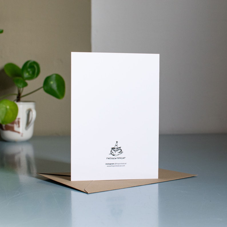 May include: A white card with a black and white illustration of a cat wearing a party hat. The text "theprintcat" is printed below the illustration, along with the text "instagram: @theprintcat" and "www.theprintcat.com".