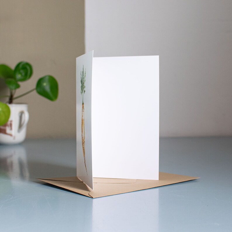 May include: A blank greeting card with a brown envelope. The front of the card features a watercolor illustration of a carrot.