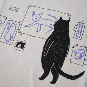 Cat gallery t-shirt | Hand screen printed on beige organic cotton tee with black and blue illustration of a cat judging his own art image 2