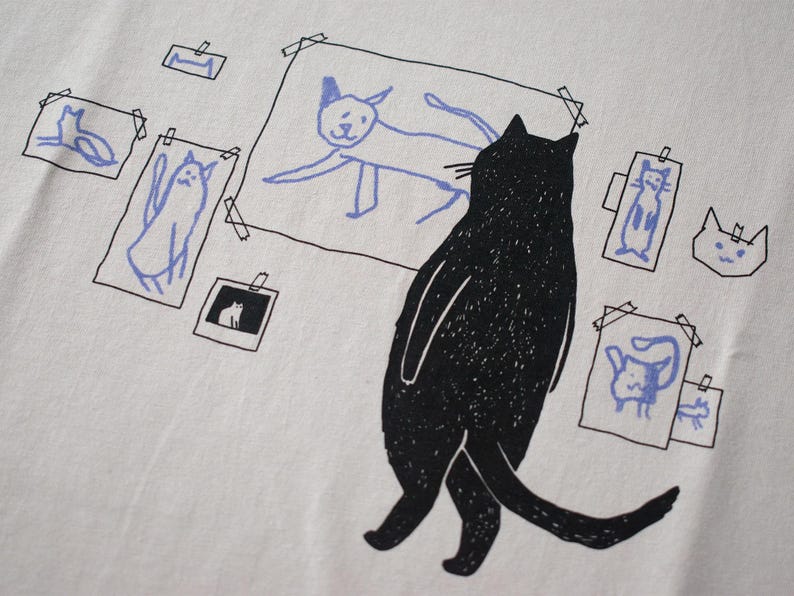 Cat gallery t-shirt | Hand screen printed on beige organic cotton tee with black and blue illustration of a cat judging his own art image 2