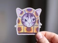 Sunflower Balaclava Cat | Cute holographic vinyl sticker of a purple tabby cat wearing a balaclava with flowers on it product logo