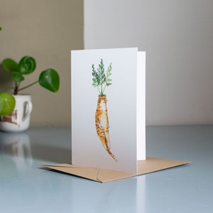 May include: A white card with a humorous illustration of an orange tabby cat with green leafy stems growing out of its head, resembling a carrot.