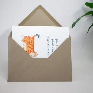 May include: A greeting card with a cartoon illustration of an orange and white cat with blue eyes. The cat is walking with its tail up in the air. The text on the card reads "Jiggle Jiggle Chonky Jiggle All The Way".