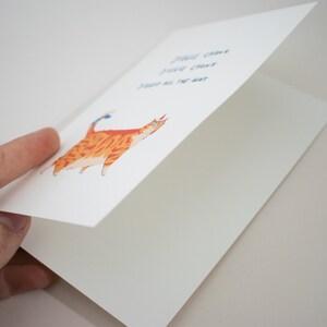 May include: A greeting card with a cartoon orange tabby cat with blue eyes and a blue bow on its tail. The text on the card reads "You can't just give up on the way".