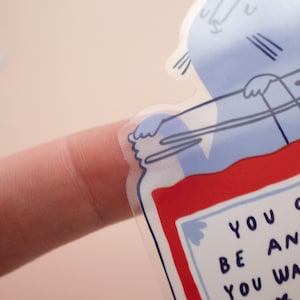 May include: A clear sticker with a blue and red illustration of a jar with a lid. The jar has a label that says "You can be anything you want".