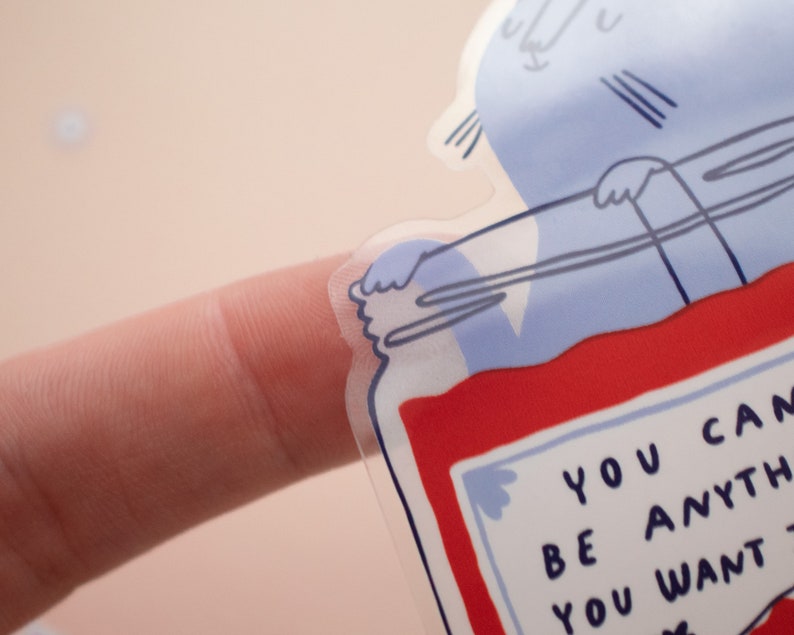 May include: A clear sticker with a blue and red illustration of a jar with a lid. The jar has a label that says "You can be anything you want".