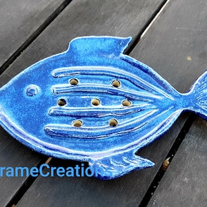Peut inclure: Un porte-savon en céramique bleu en forme de poisson avec des trous de drainage. Le plat a une surface texturée et une finition brillante.