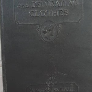 May include: A black book with the title "Designing and Decorating Clothes" embossed on the front cover. The book is published by the Woman's Institute of Domestic Arts and Sciences in Scranton, Pennsylvania.