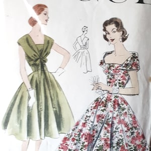 Op de afbeelding: Vintage Vogue naaipatroon voor een jurk, met twee modellen die verschillende stijlen dragen. Het patroonnummer is 8918 en de borstomvang is 32. Een model draagt een groene jurk met een strik in de taille, terwijl het andere een jurk met bloemenprint en een vierkante halslijn draagt.