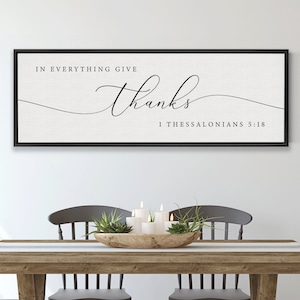 Puede incluir: Una impresión enmarcada con el texto "In everything give thanks 1 Thessalonians 5:18" en un marco negro colgado en una pared blanca sobre una mesa de madera con cuatro sillas.