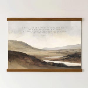 May include: A framed landscape print featuring a quote from Psalm 121:1-2. The artwork shows a valley with rolling hills in shades of brown, beige, and grey. The text is in a light grey font and is held by wooden bars.