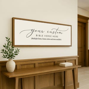 May include: A rectangular wooden framed sign with the text "your custom BIBLE VERSE HERE" in black script. The sign is mounted on a light-colored wall above a wooden console table. The text below the main text reads "(Multiple fonts, frame colors and sizes available.)"