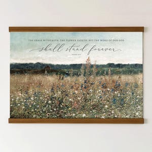 May include: A framed print depicting a field of wildflowers under a light blue sky. The artwork includes the text "THE GRASS WITHERETH, THE FLOWER FADETH: BUT THE WORD OF OUR GOD shall stand forever."