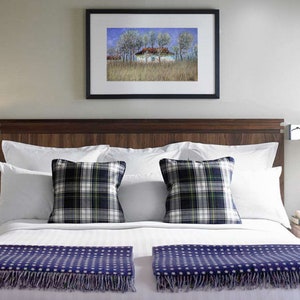 May include: A white bed with a wooden headboard and two white pillows with plaid throw pillows. A blue and white patterned throw is on the bed. There is a framed picture above the headboard and a nightstand on each side of the bed.