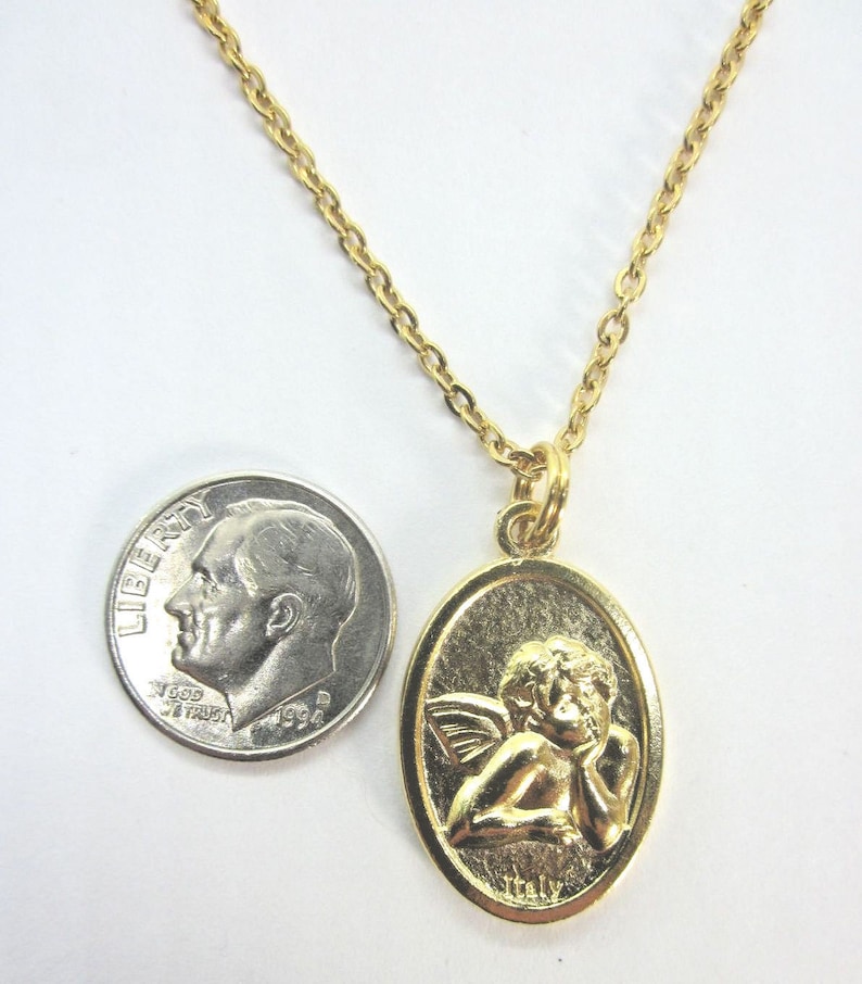 Puede incluir: Un collar de cadena de oro con un colgante ovalado de oro que presenta un querub&iacute;n con alas. El colgante tiene la palabra "Italia" inscrita en la parte inferior.