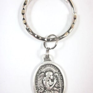 Op de afbeelding: Zilverkleurige sleutelhanger met een gehamerde ring en een ovale hanger. De hanger toont de aartsengel Gabriël met bloemen, met de tekst "ST. GABRIEL ARCHANGEL PRAY FOR US". Religieus thema.