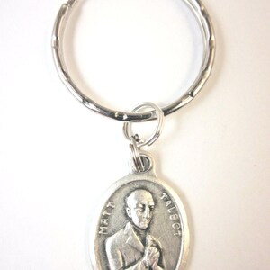 May include: Silver key chain with a round metal ring and a silver oval charm featuring a black and white image of a man with the text "MATT TALBOT" on the charm.