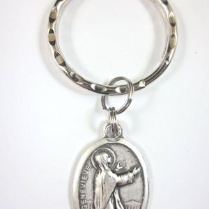 May include: Silver key chain with a round metal ring and a silver oval charm featuring a religious image of Saint Genevieve. The charm has the text "St Genevieve" inscribed on it.