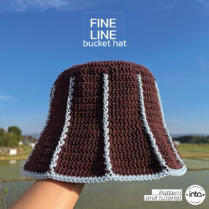 Könnte beinhalten: Gehäkelter Eimerhut in Braun mit hellblauen Verzierungen und vertikalen Streifen. Der Hut trägt den weißen Schriftzug "FINE LINE bucket hat". Das Bild enthält auch den Text "Pattern and tutorial".