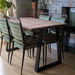 Pode incluir: Uma mesa de jantar de madeira com uma estrutura de metal preto e quatro cadeiras estofadas verdes. A mesa tem um acabamento de madeira rústico e as cadeiras têm um design simples.