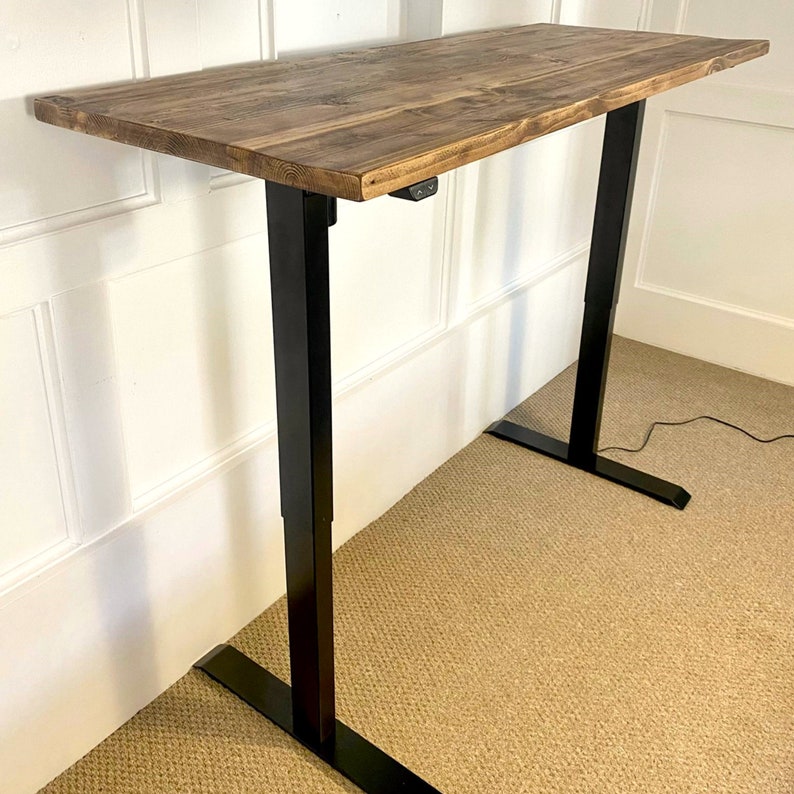 May include: A standing desk with a rustic wood top and black metal legs. The desk is height adjustable and has a power outlet on the side.