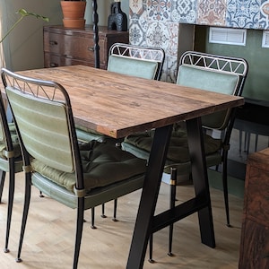 May include: A wooden dining table with a black metal A-frame base. The table has a rustic wood finish and is surrounded by four green upholstered chairs with metal frames.
