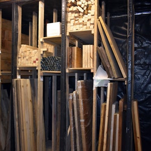 May include: A wooden storage rack filled with various sizes and types of wood planks. The planks are stacked neatly and organised by size and type. The rack is made of metal and has a black finish.