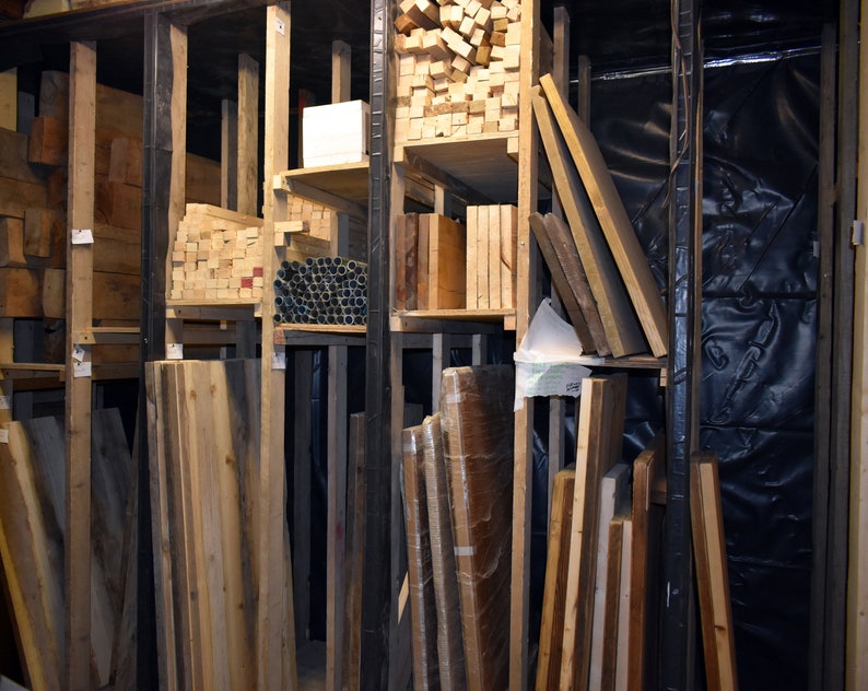 May include: A wooden storage rack filled with various sizes and types of wood planks. The planks are stacked neatly and organised by size and type. The rack is made of metal and has a black finish.