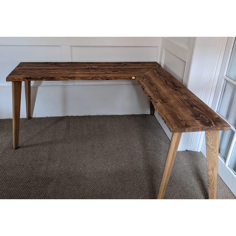 May include: A corner desk made of reclaimed wood with a dark brown stain. The desk has a simple design with angled legs and a wide, rectangular top.